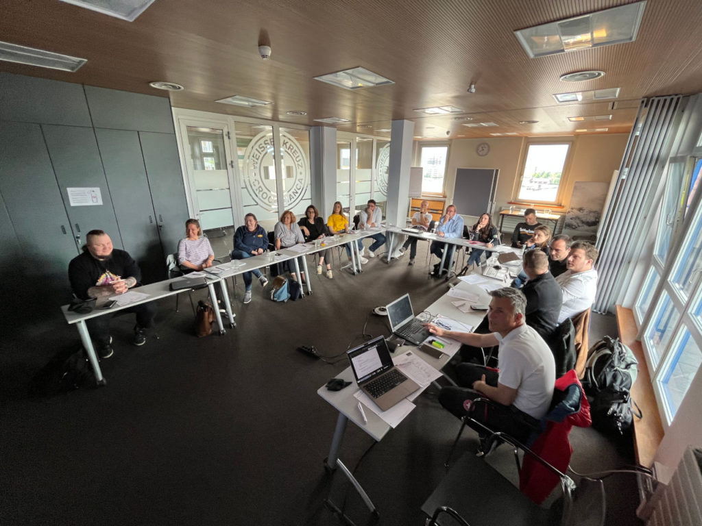 View of the members of the project group sitting in a U-shaped table and chair configuration during a presentation, view from the presentation screen.